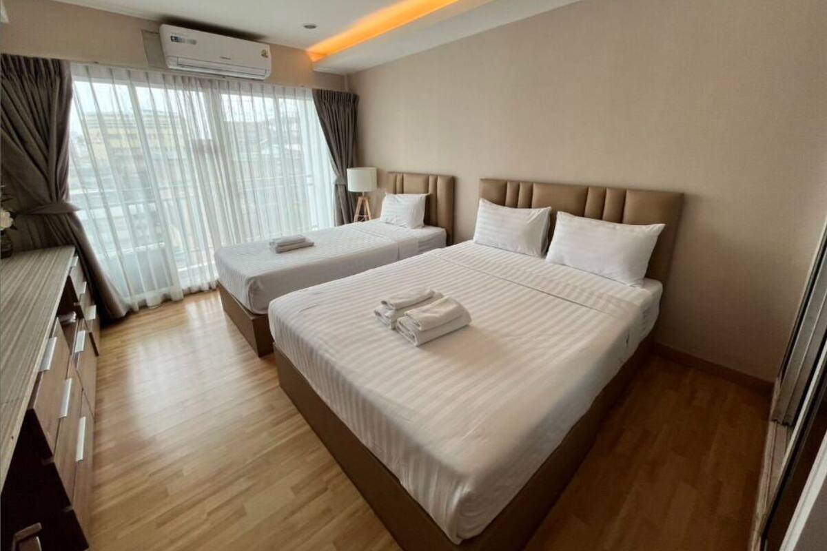 A hotel room with two beds, a desk, and a window with curtains.