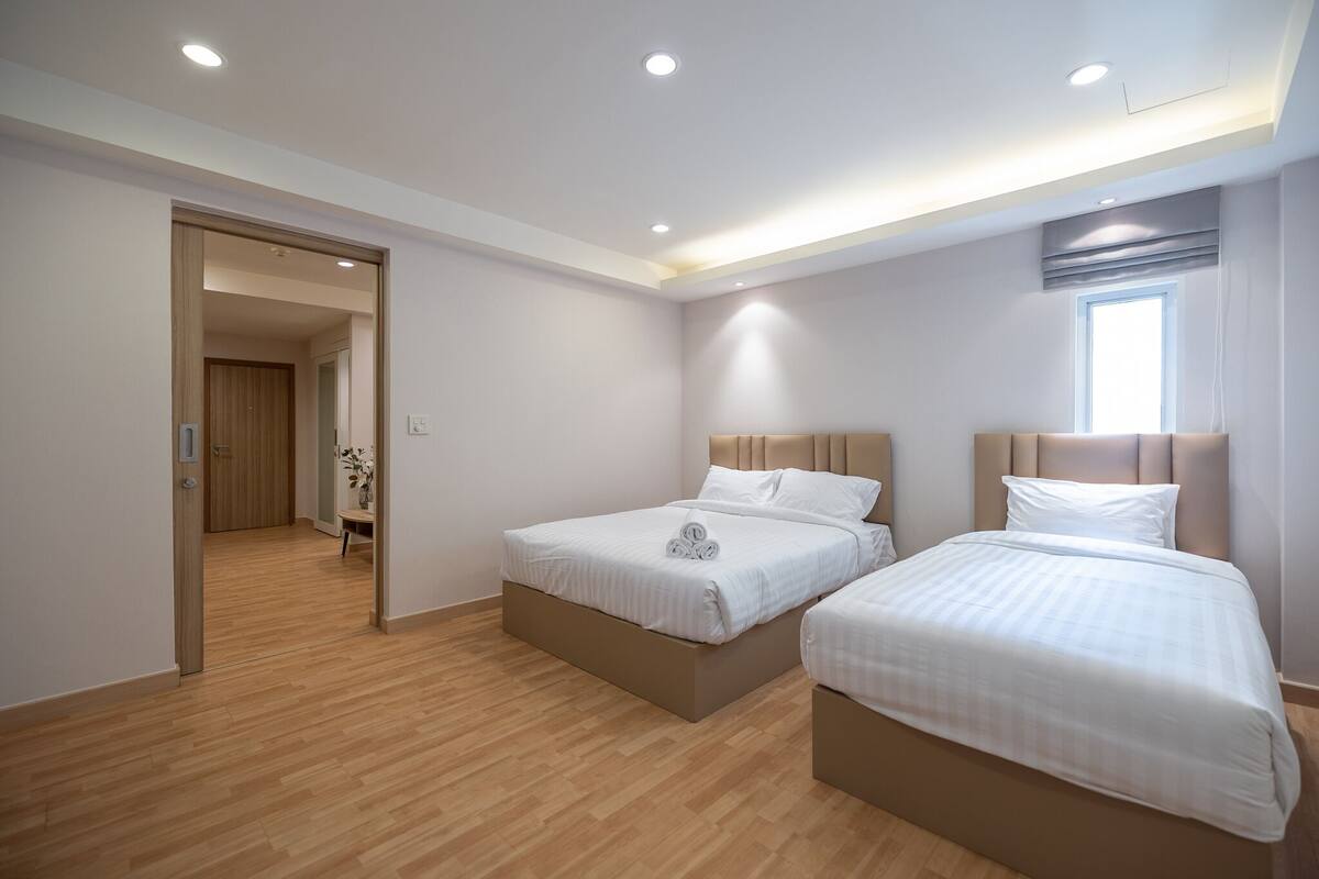 A modern hotel room with two beds, wooden flooring, and a large window.
