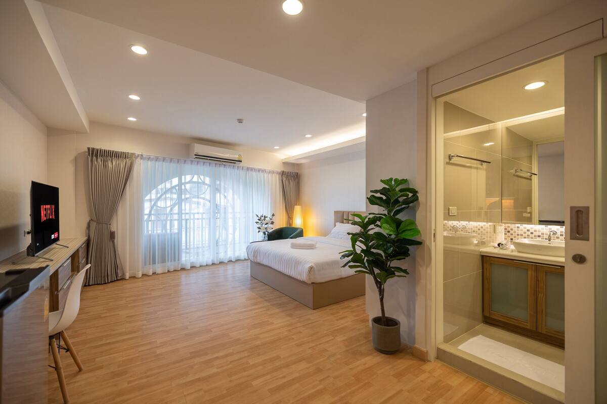 A modern hotel room with a bed, desk, TV, and a bathroom with a glass shower.