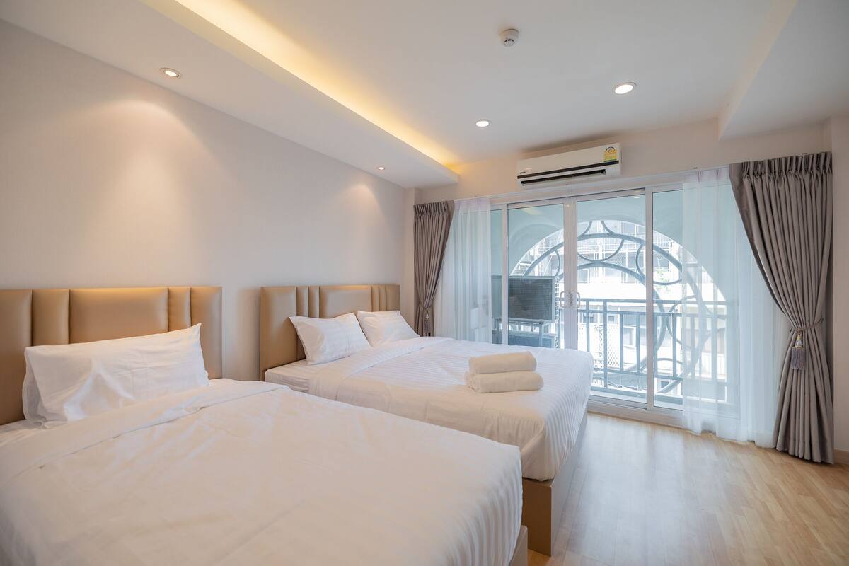 A hotel room with two beds, a large window with curtains, and an air conditioning unit.