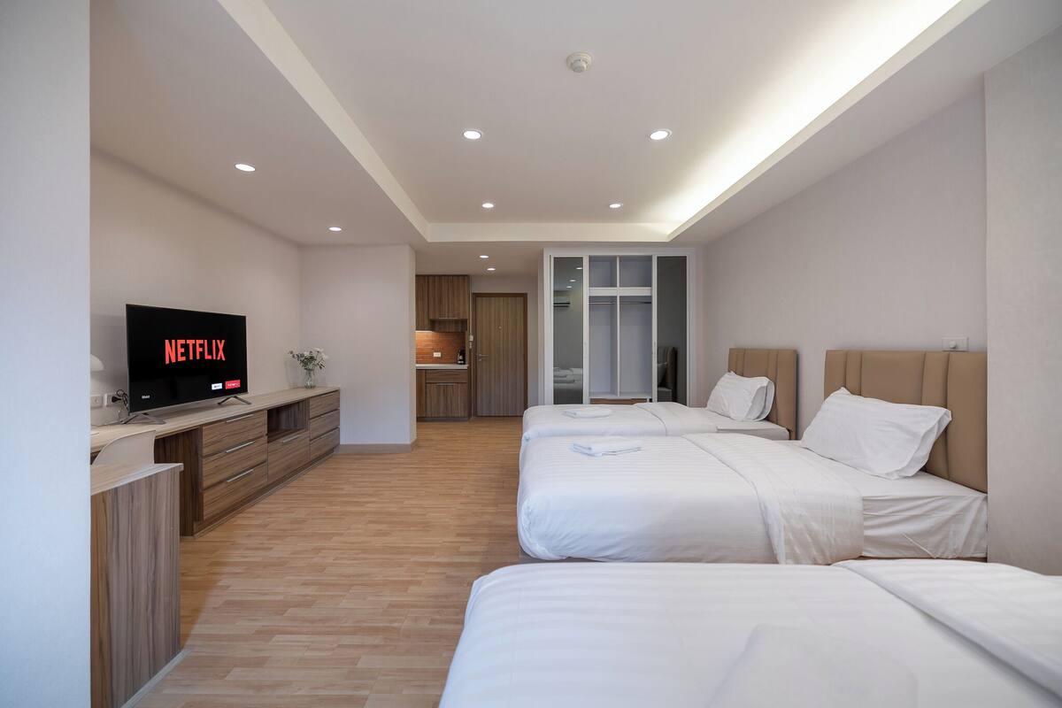 A modern hotel room with two beds, a TV displaying 'NETFLIX', a kitchenette, and a sliding door closet.
