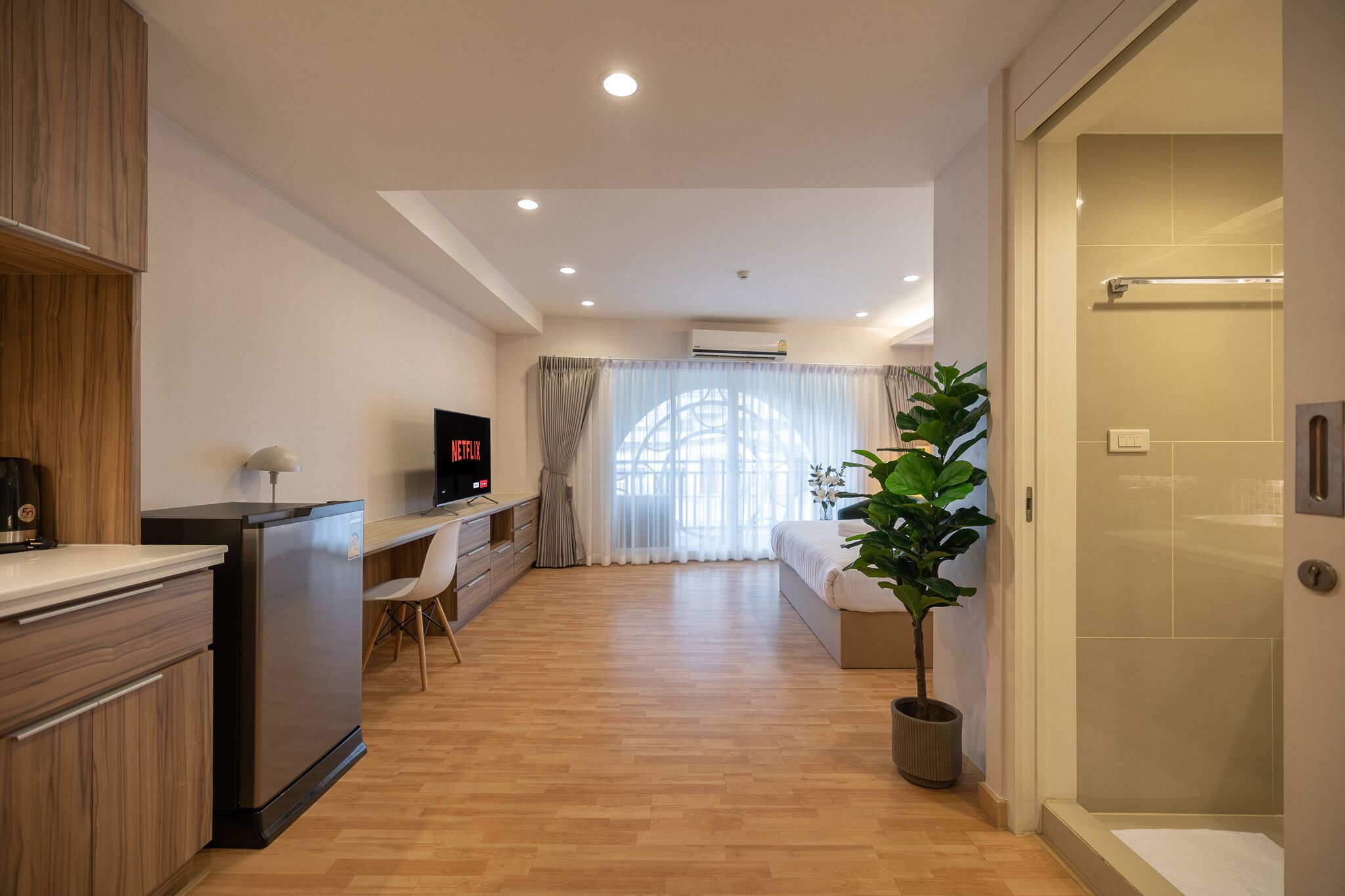 A modern hotel room with a kitchenette, a TV, a desk, a bed, and a shower area.