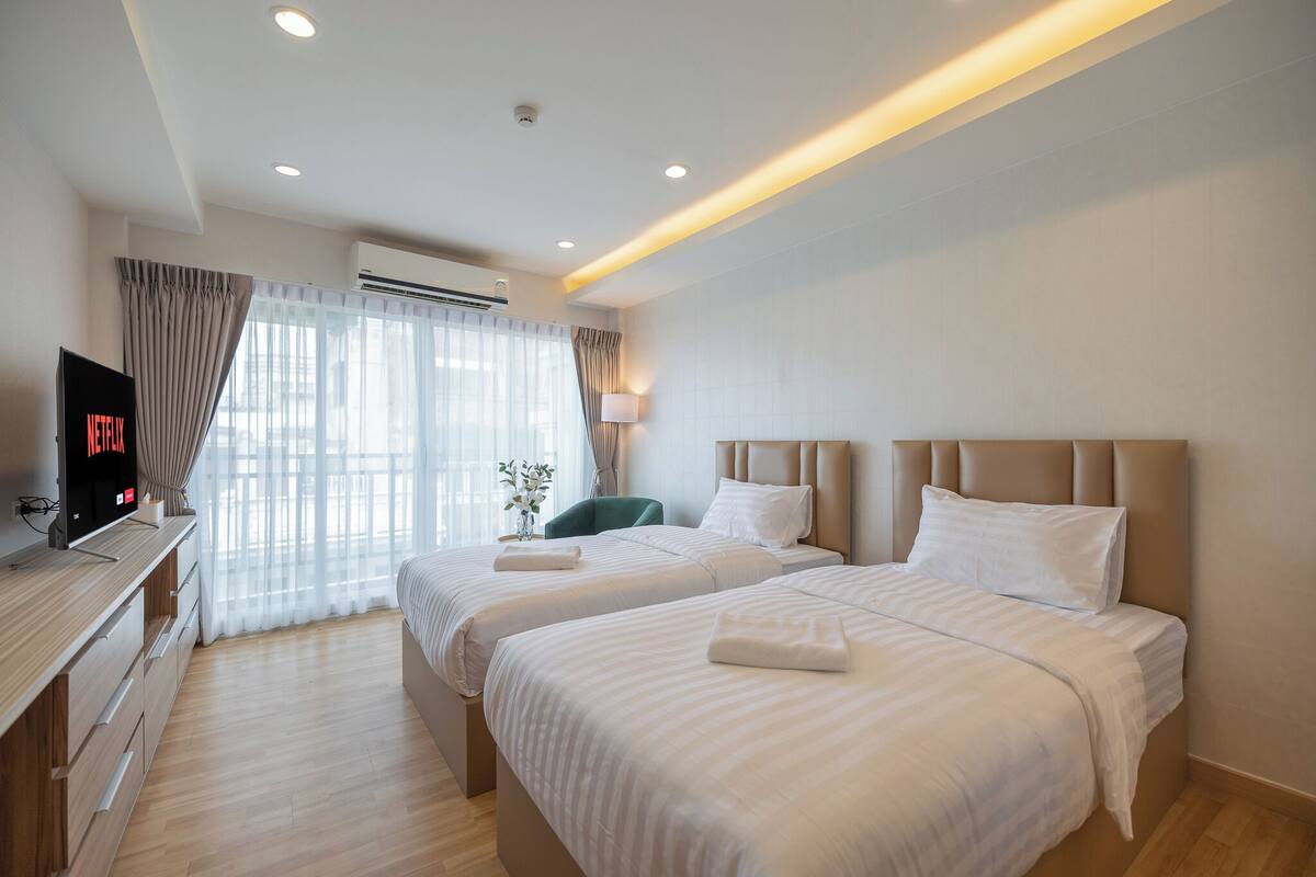 A hotel room with two beds, a TV, a desk, and a window with curtains.