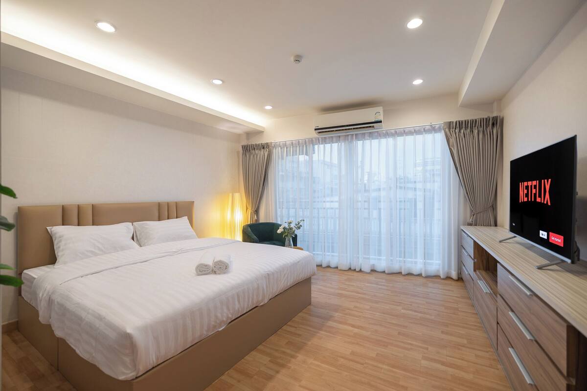A modern hotel room with a large bed, a TV, and a wooden floor.
