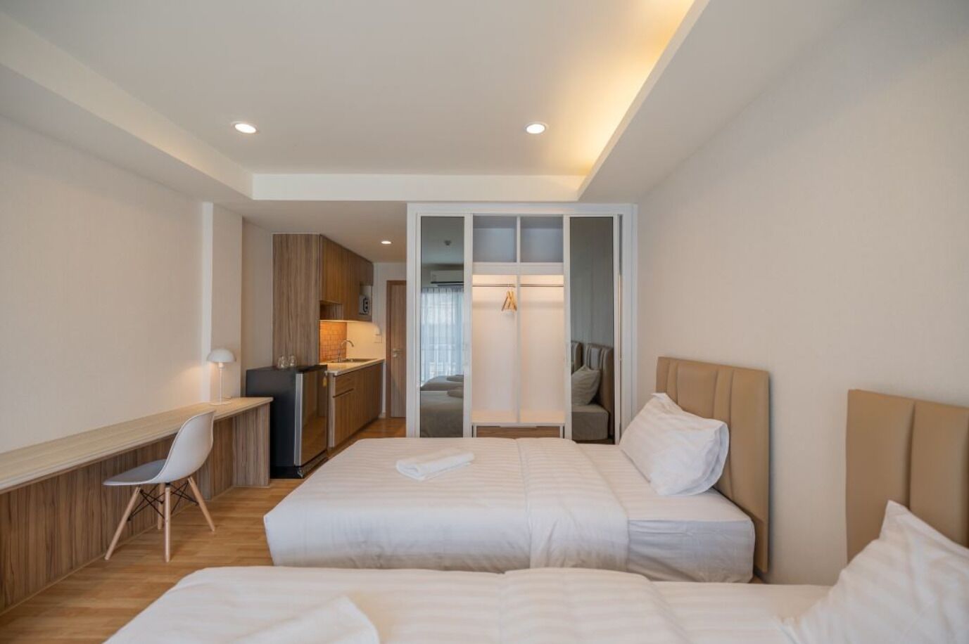 A modern hotel room with two beds, a desk, and a kitchenette.