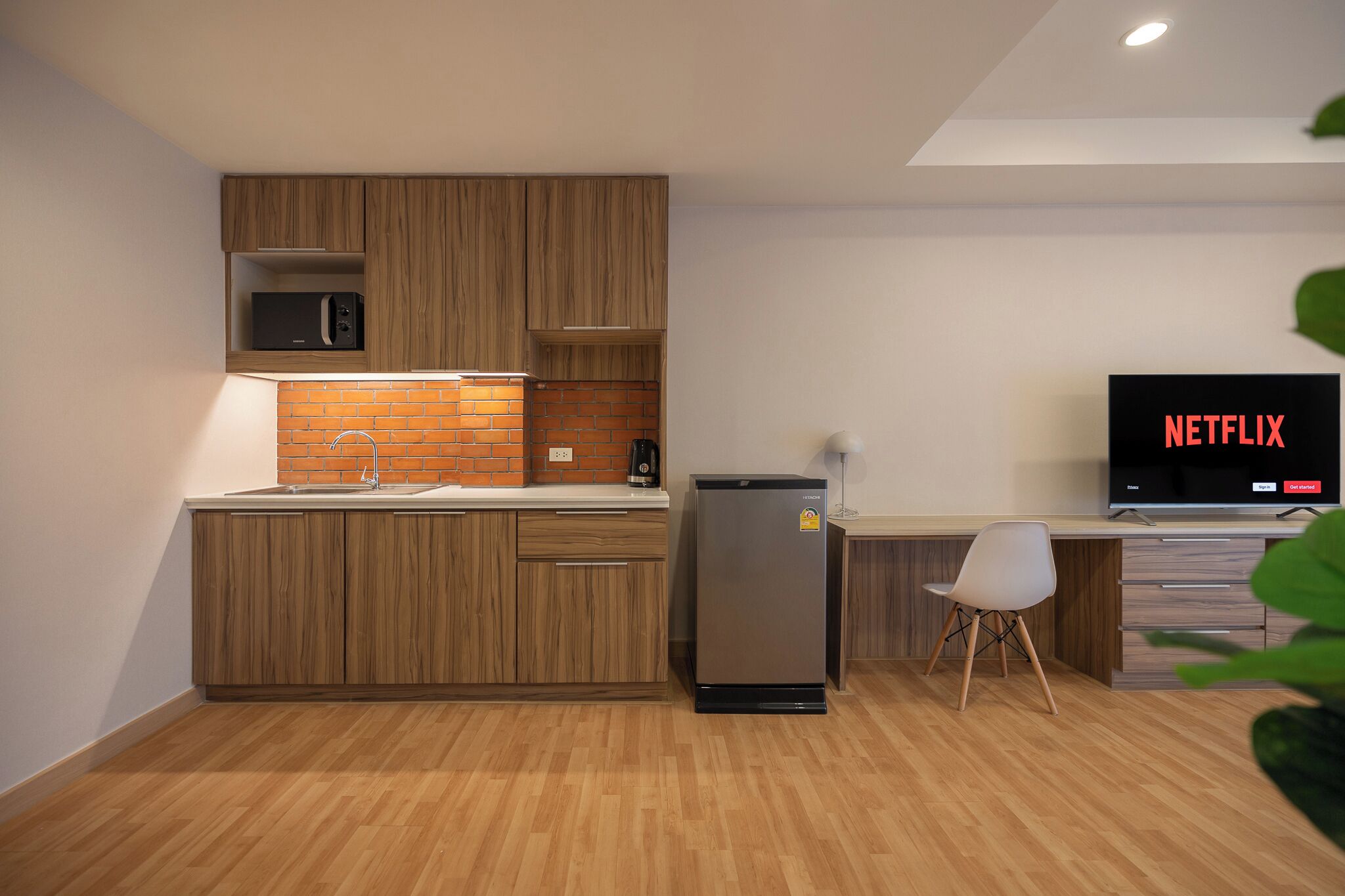 Eine moderne Küche mit Holzschränken, einer eingebauten Mikrowelle, einem Kühlschrank und einem Essbereich mit einem Stuhl.