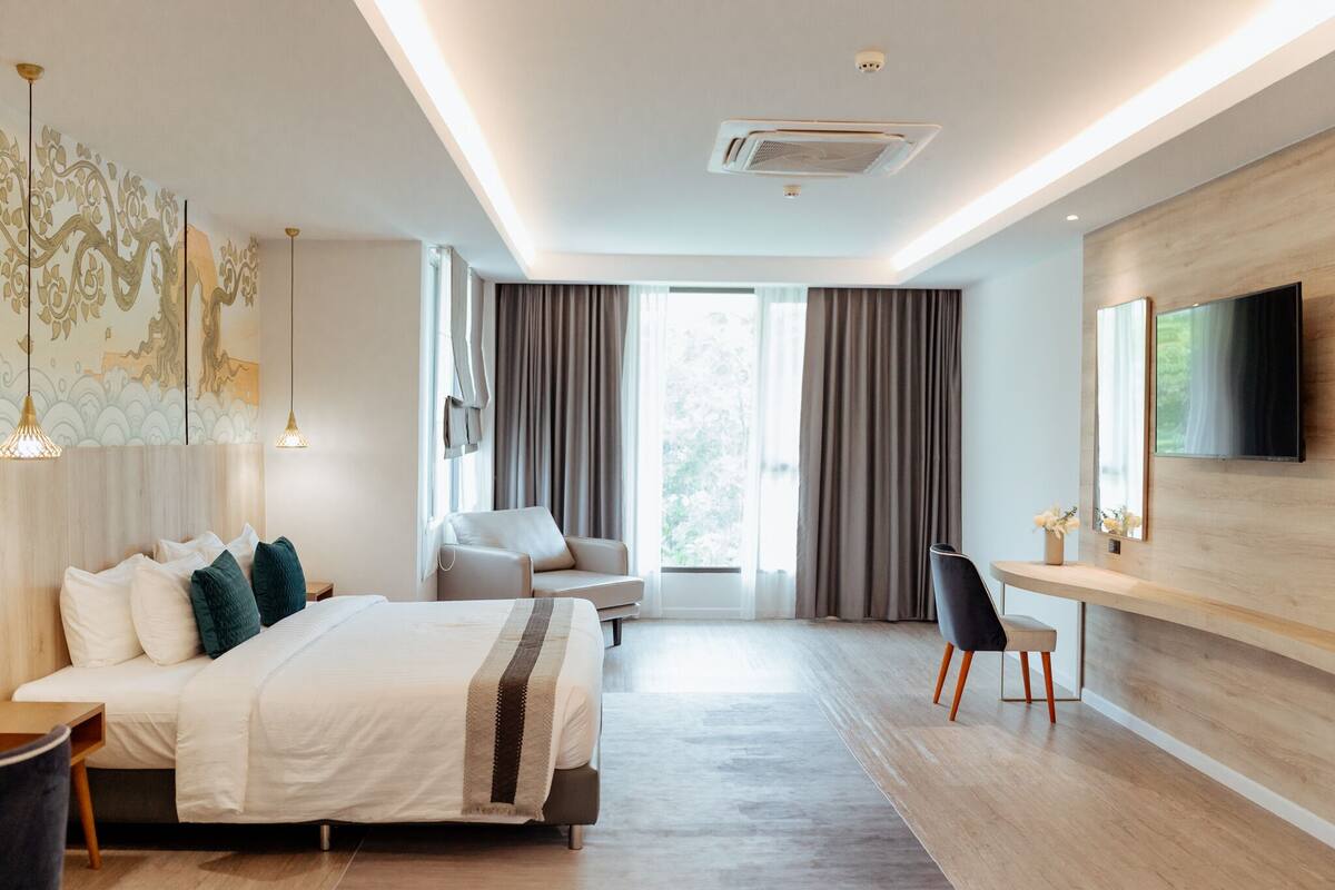 A modern hotel room with a large bed, a desk, a chair, and a TV mounted on the wall.