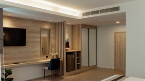 A modern bedroom with a large bed, a desk with a chair, a TV mounted on the wall, and a wardrobe. - RUS Hotel&Convention (Ayutthaya)