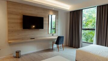 Una habitación de hotel moderna con un televisor grande montado en una pared de madera, un escritorio con una silla, una cama y una ventana con cortinas.