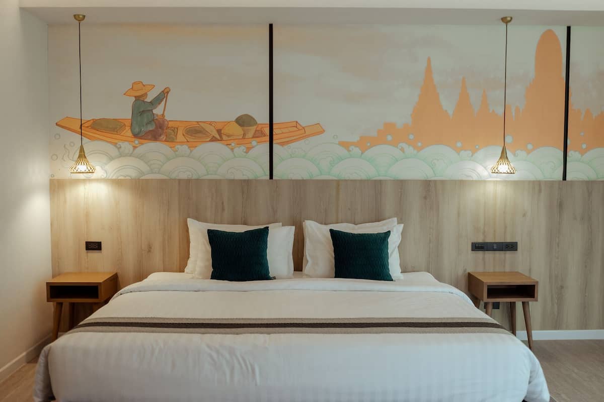 A modern hotel room with a large bed, two bedside tables, a wooden headboard, and a wall mural depicting a person in a boat.
