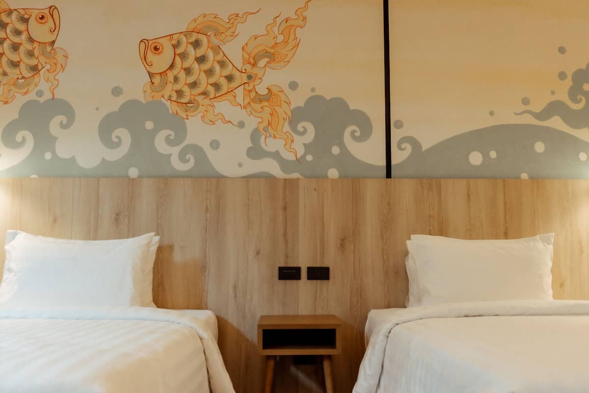 A hotel room with two beds, a wooden headboard, and a decorative wall with fish and wave patterns.