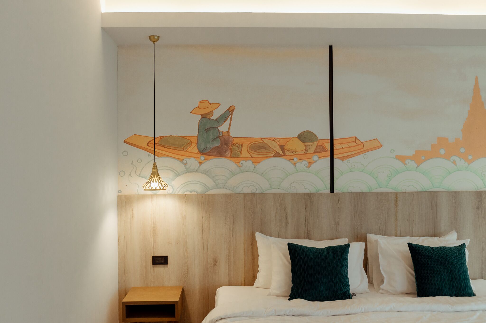 Habitación de hotel con cabecera de madera, cama con almohadas blancas y verde oscuro, y un mural en la pared que muestra a una persona en un bote.