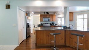 Une cuisine moderne avec des meubles en bois, un réfrigérateur en acier inoxydable, un four à micro-ondes et un grand îlot central doté de tabourets de bar.