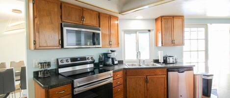 A compact kitchen with wooden cabinets, a microwave, an oven, a dishwasher, and a ceiling fan.