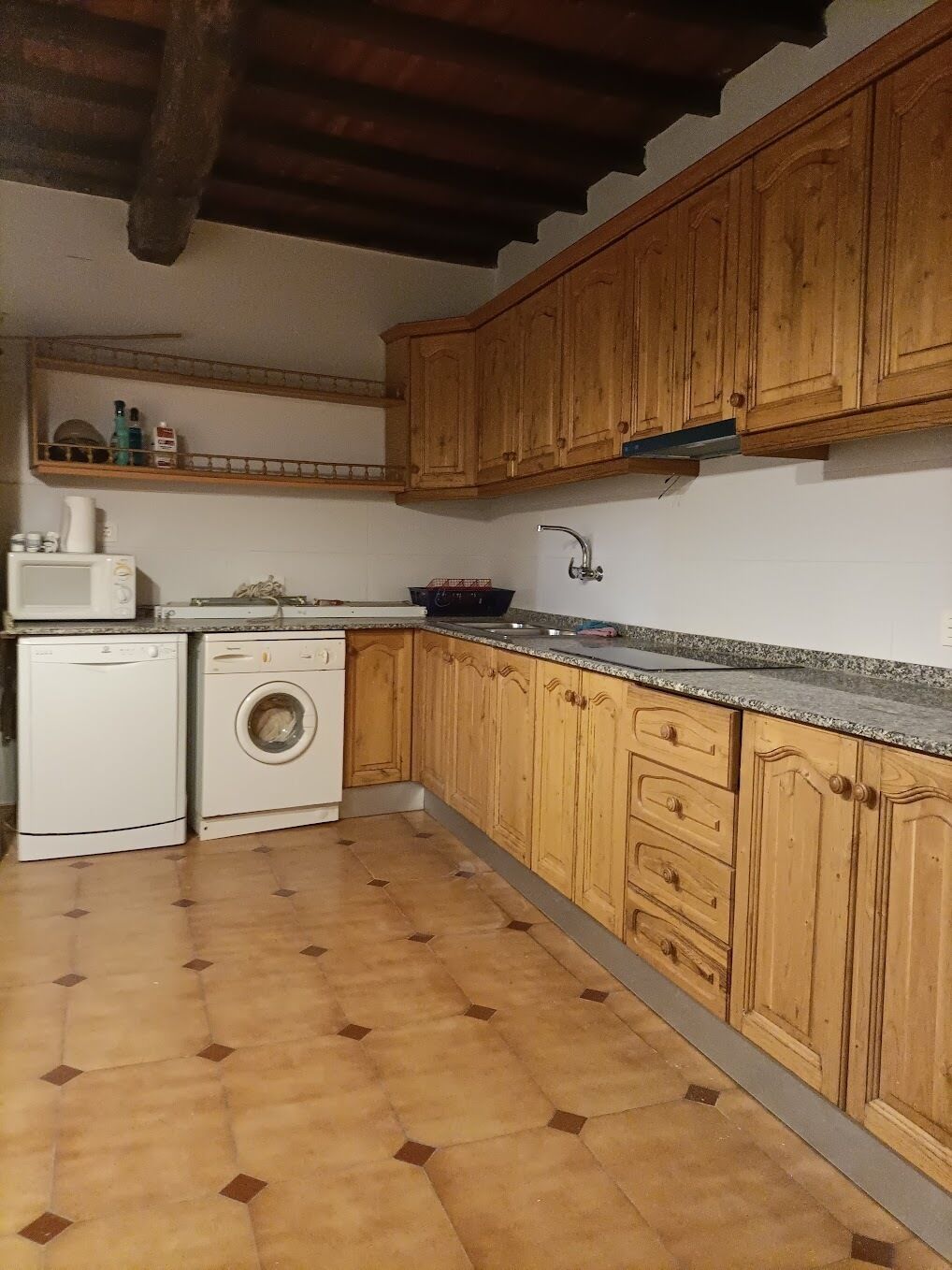 Una cocina con armarios de madera, microondas, lavadora y pileta.