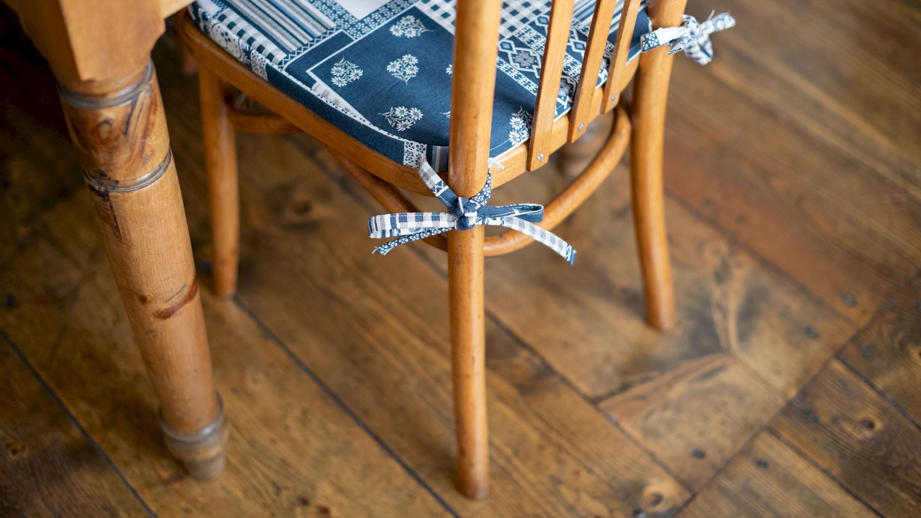 Une chaise en bois avec un coussin à motifs et un ruban à carreaux bleus et blancs noué autour du dossier.