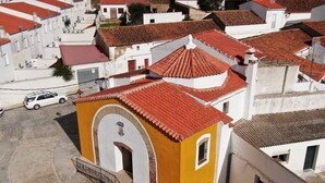 Un bâtiment jaune avec un toit recouvert de tuiles rouges, des murs blancs et une petite entrée en arc de cercle.