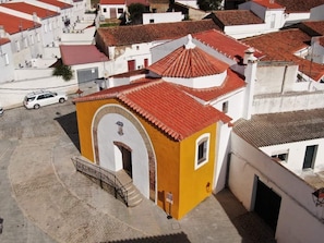 A yellow building with a red-tiled roof, white walls, and a small arched entrance.