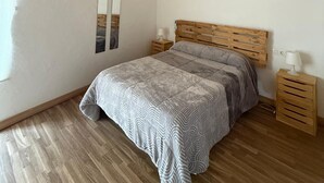 Une chambre avec un plafond en bois, un lit recouvert d’une couvre-lit à motifs, une table de chevet avec une lampe et un climatiseur fixé au mur.