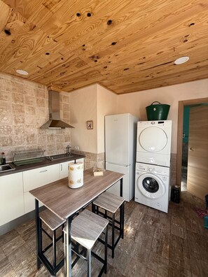 A compact kitchen with a wooden ceiling, a sink, a stove, a refrigerator, and a washing machine.