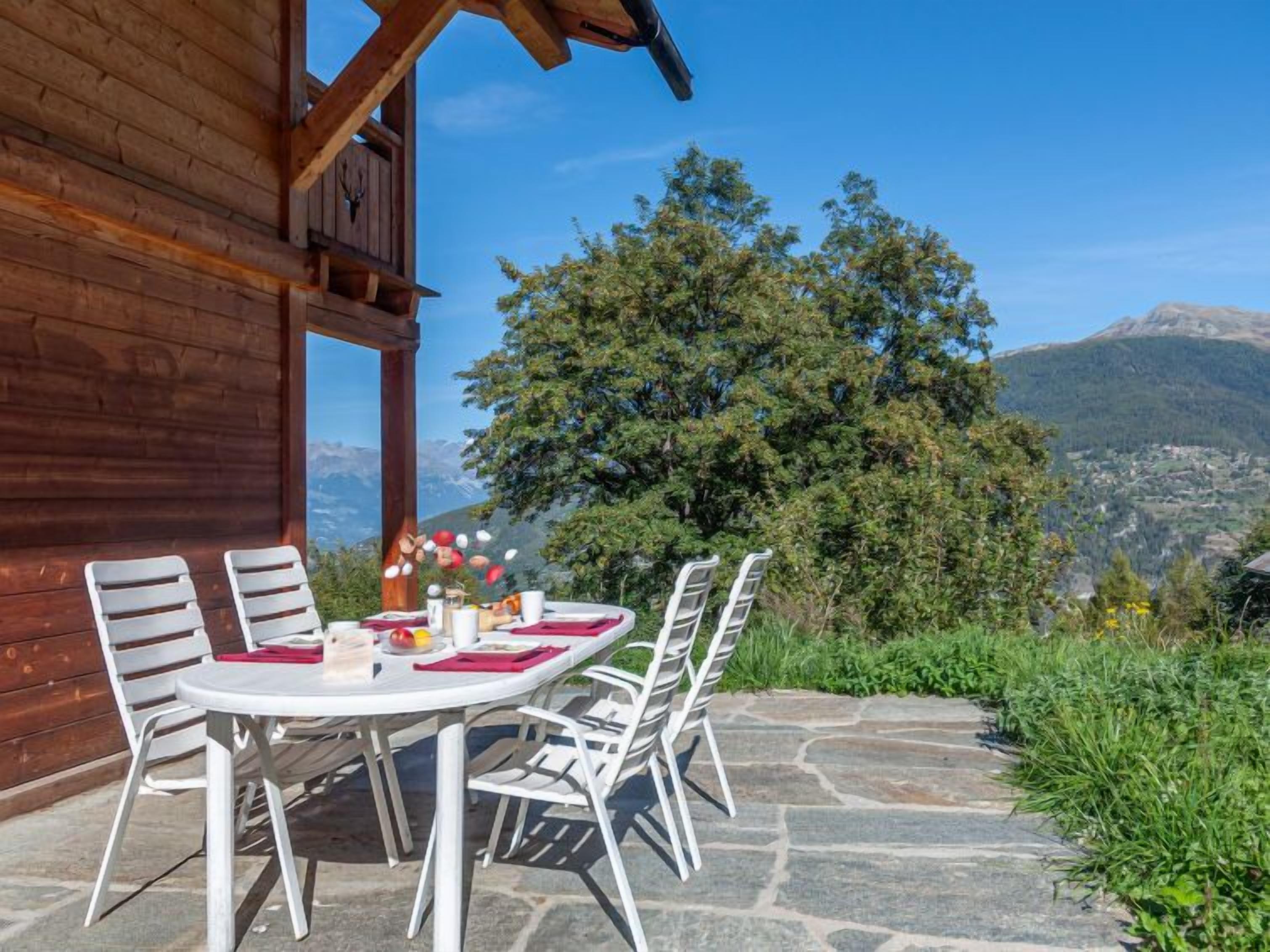 A wooden cabin with a stone patio, white chairs, and a table set for dining.