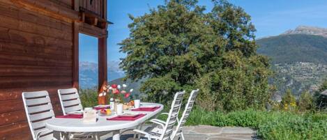 A wooden cabin with a stone patio, white chairs, and a table set for dining.