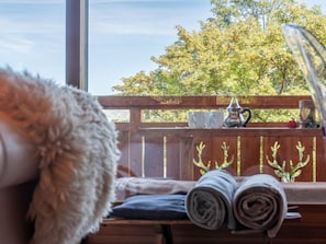 Une pièce avec un banc en bois, une fenêtre donnant sur des arbres et un objet recouvert de fourrure posé sur le sol.