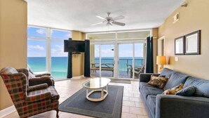A living room with a view of the ocean, a ceiling fan, a flat-screen TV, and a sofa with cushions. - Jade East Towers 1120 (Destin)