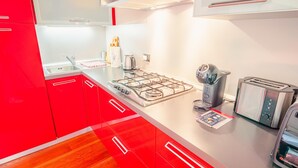 A modern kitchen with red cabinets, a gas stove, a kettle, and a toaster. - Old Town Alley - Italian Homing (Desenzano del Garda)