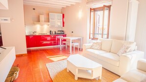 A modern living room with a white sofa, a small white table, and a kitchen area with red cabinets and white appliances. - Old Town Alley - Italian Homing (Desenzano del Garda)