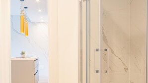 A modern bathroom with a glass shower enclosure, marble walls, and a minimalist design.