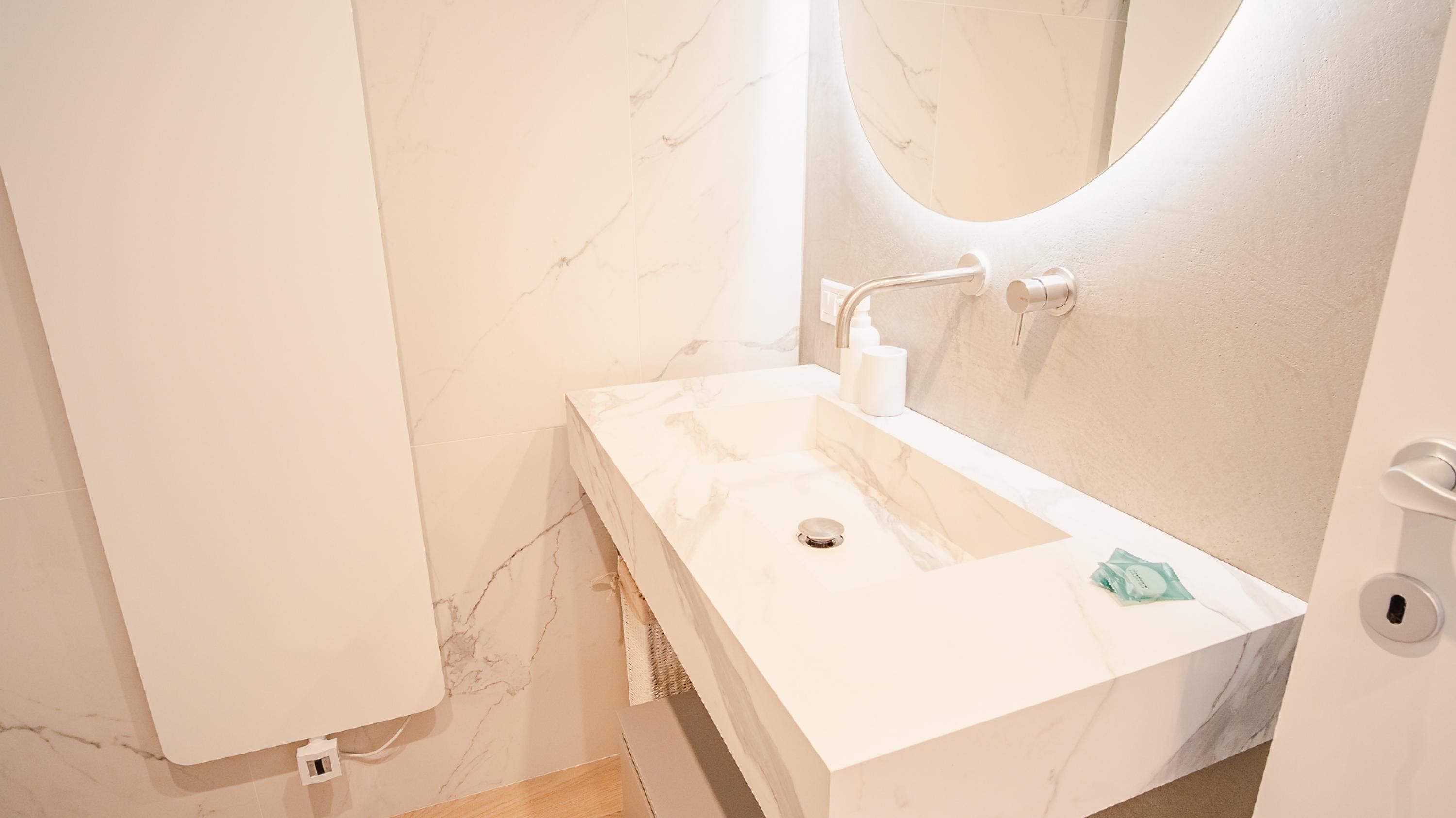 A bathroom with a white marble sink, a mirror, and a towel dispenser.