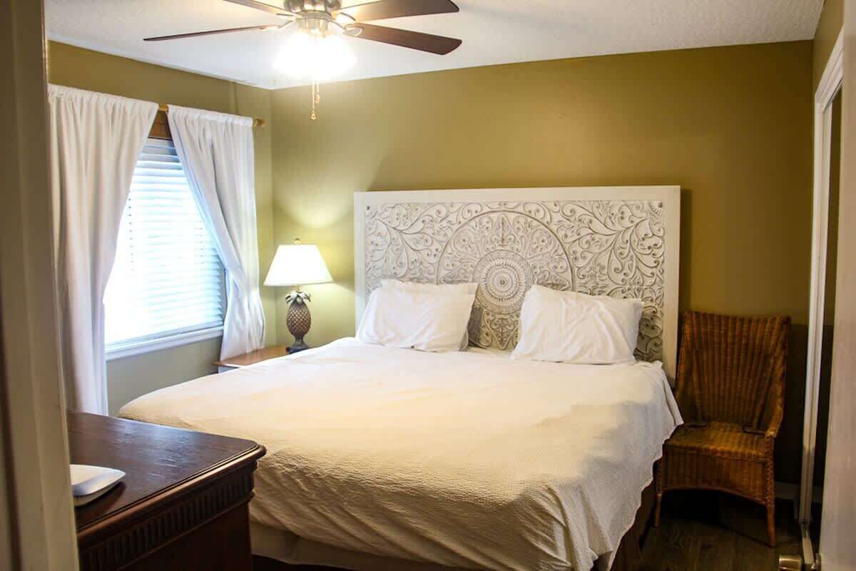 A bedroom with a large bed, a ceiling fan, a nightstand, a lamp, and a chair.