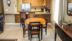 A kitchen with wooden cabinets, a central island, a refrigerator, and a dining area with chairs and a table. - Gulf-front condo on Okaloosa Island with balcony and views (Fort Walton Beach)