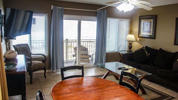 A living room with a wooden dining table, two chairs, a sofa, a TV, and a ceiling fan. - Gulf-front condo on Okaloosa Island with balcony and views (Fort Walton Beach)