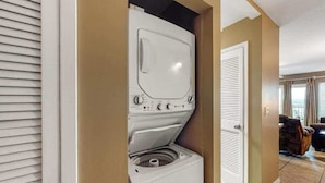 A compact, modern laundry room with a built-in washer and dryer, a door leading to a living area, and a tiled floor. - Gulf-front condo on Okaloosa Island with balcony and views (Fort Walton Beach)