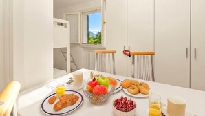 A breakfast table with croissants, fruit, and juice, a window with a mountain view, and white furniture. - Porto Letizia Begonia 7, Porlezza, Italy (Porlezza)