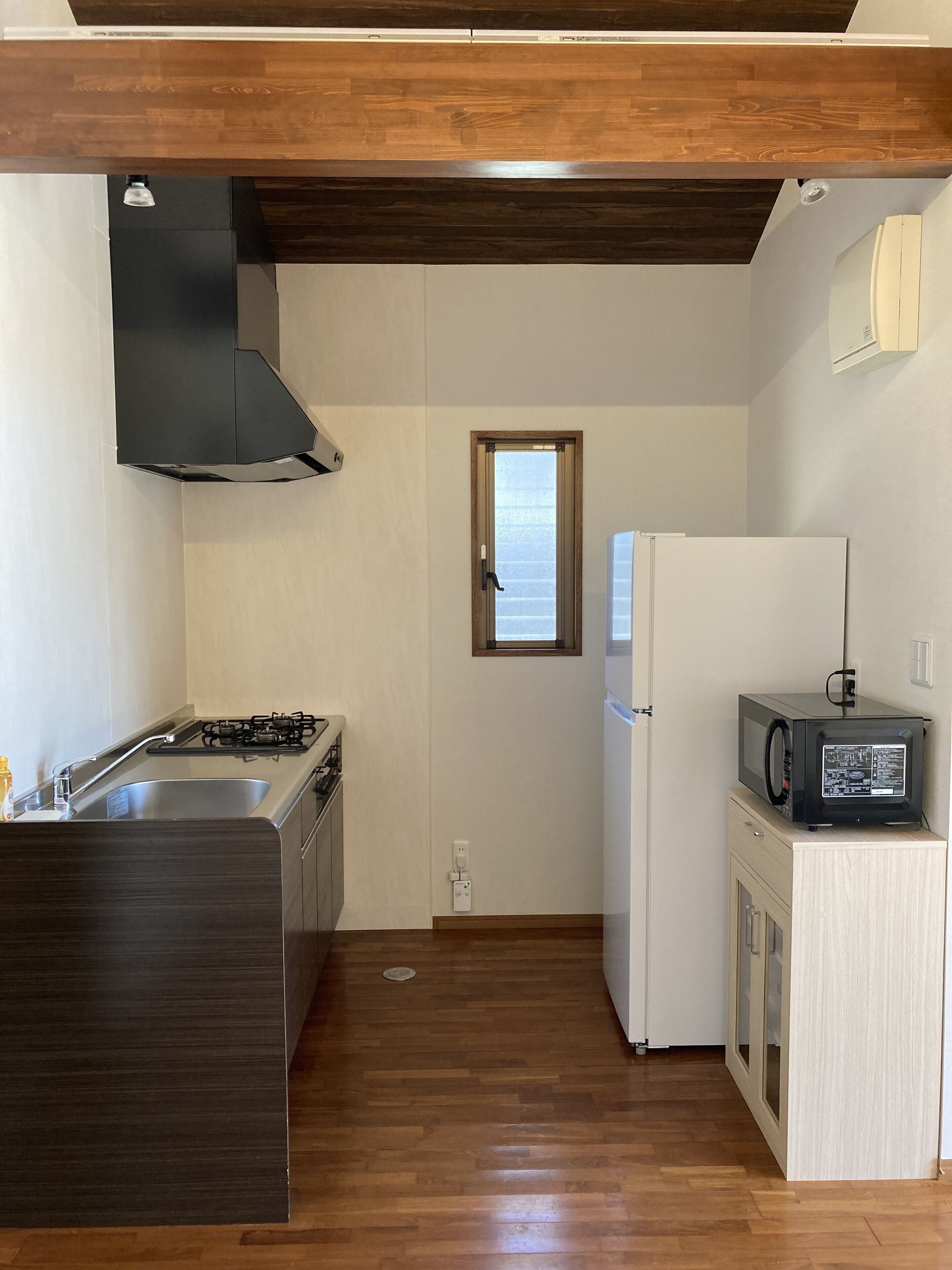 A compact kitchen with a gas stove, a microwave, a refrigerator, and a window.