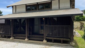 A two-story building with a sloped roof, large windows, and a covered porch area. - Pension Shimakaze (Motobu)