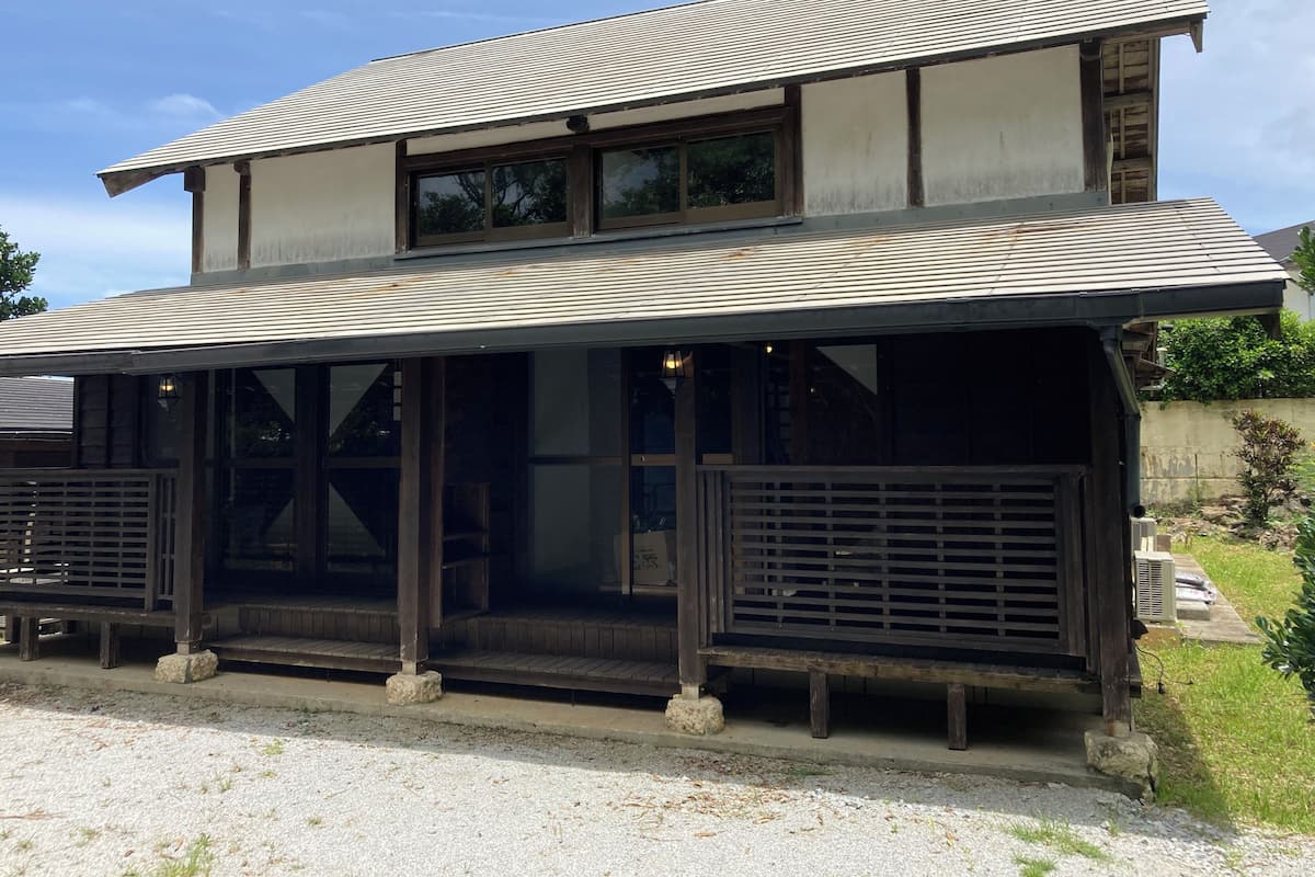 A two-story building with a sloped roof, large windows, and a covered porch area.