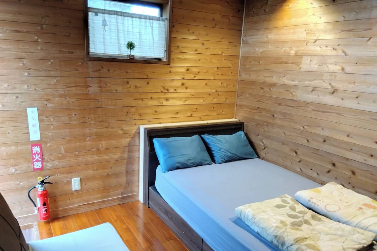 A small, wooden-paneled room with a bed, a window, and a fire extinguisher.
