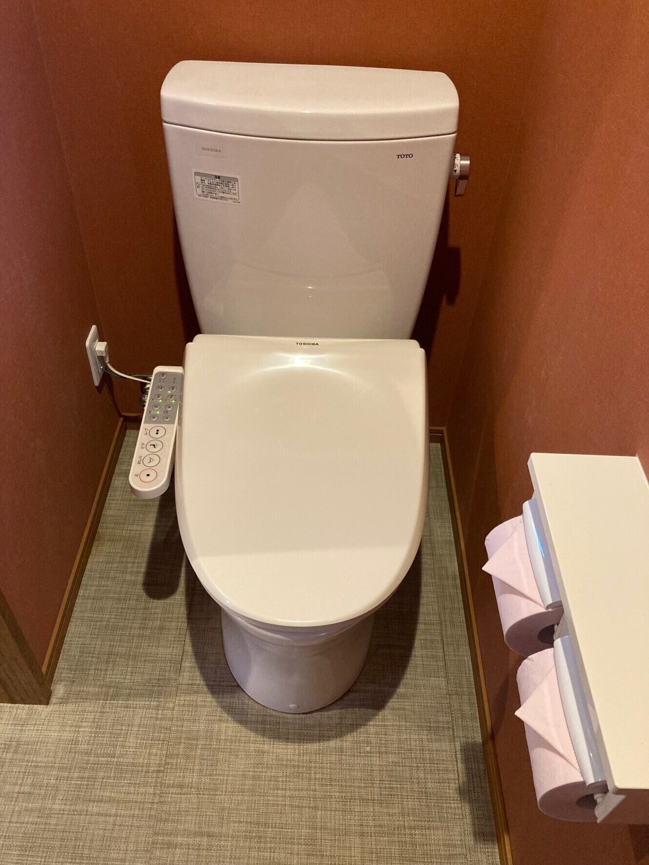 A toilet with a control panel, a tissue dispenser, and a toilet paper holder.
