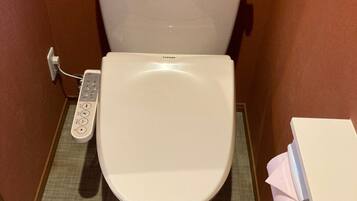 A toilet with a control panel, a tissue dispenser, and a toilet paper holder.