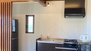 A modern kitchen with wooden flooring, a built-in stove, and a black range hood. - Pension Shimakaze (Motobu)