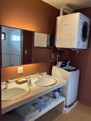A modern bathroom with a double sink, a large mirror, a built-in washing machine, and a towel rack. - Pension Shimakaze (Motobu)