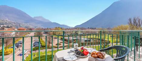 A balcony with a table set for breakfast, overlooking a mountainous landscape and a parking area.