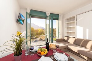 A balcony with a dining table set for two, a sofa, and a TV mounted on the wall. - Porto Letizia S1, Porlezza, Italy (Porlezza)