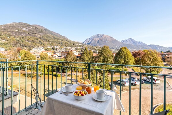 A balcony with a table set for breakfast, overlooking a mountainous landscape.