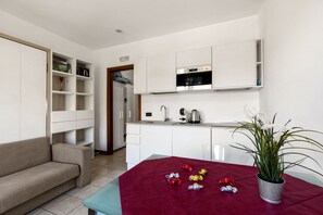 A modern kitchen with white cabinetry, a dining table with a red tablecloth, and a potted plant.