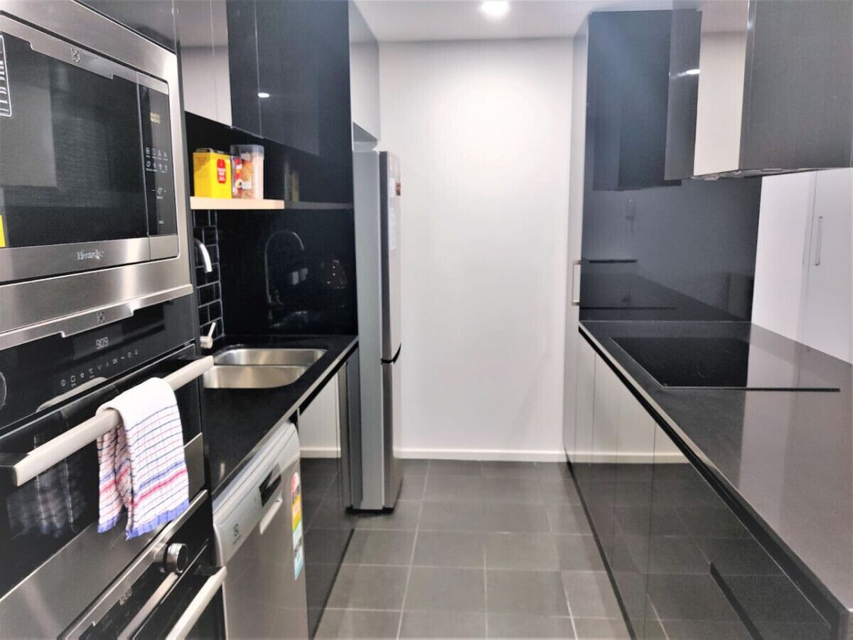 Uma cozinha moderna com eletrodomésticos de aço inoxidável, bancada preta e piso de azulejos cinzas.